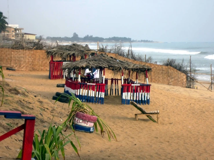 small hut on beach with colorful benches and tiki huts