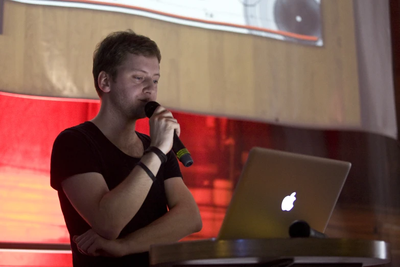 man in black t - shirt holding a microphone while looking at laptop