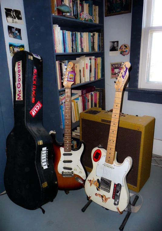 two guitars are shown sitting next to a guitar case