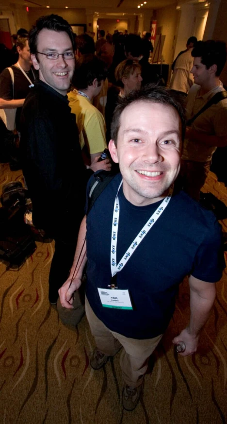 two men in a crowded building smile at the camera