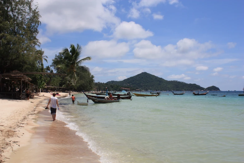 people walking along a beach with boats on the water