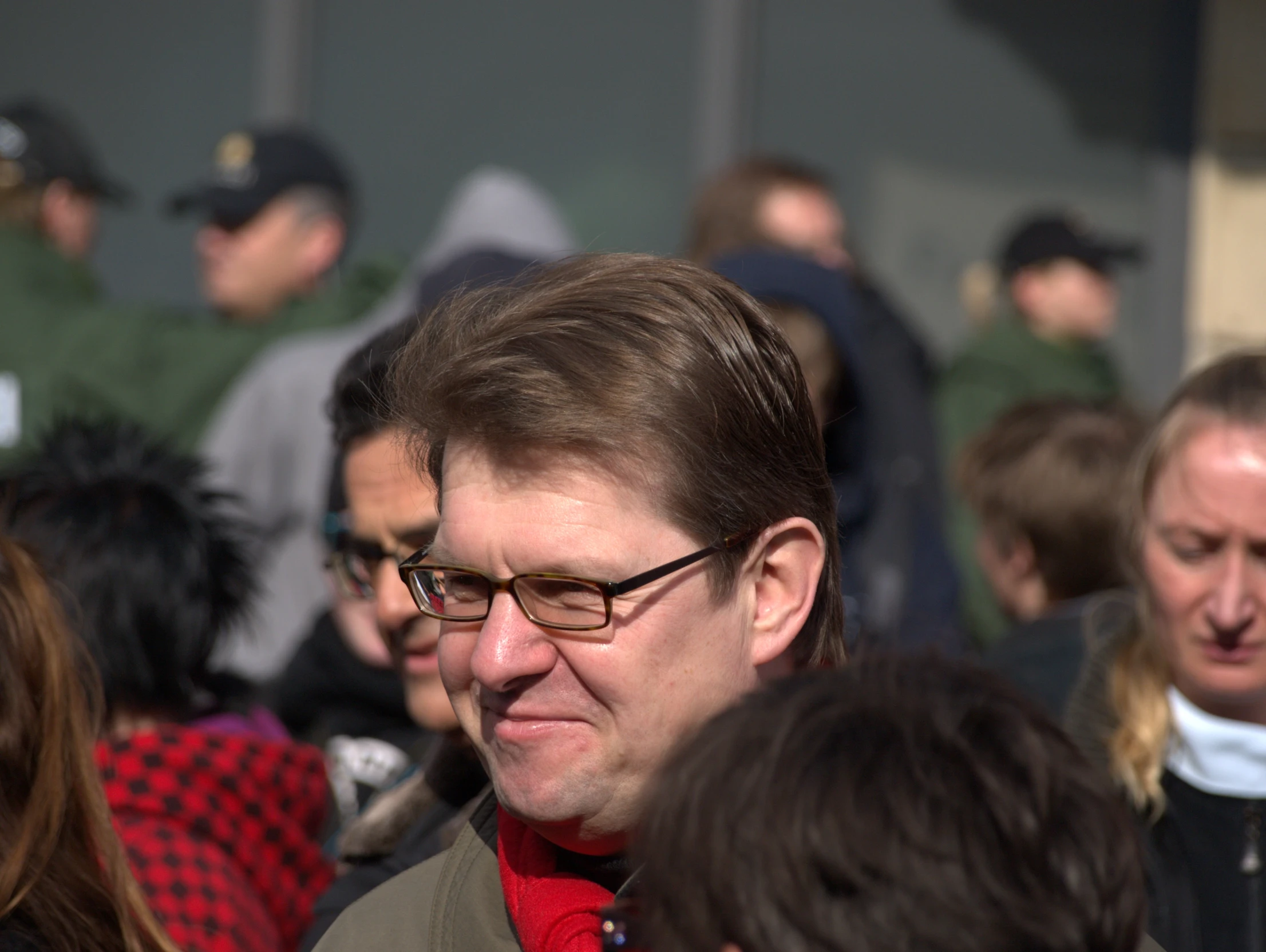 a man with glasses and a suit standing in front of some people