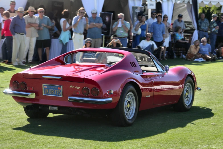 a sports car parked on a lush green field with a crowd of people watching