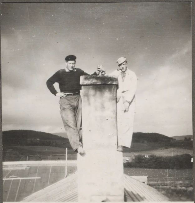 black and white pograph of two men on a metal pillar