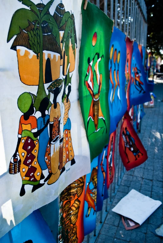 several different paintings are hung on clothes racks outside