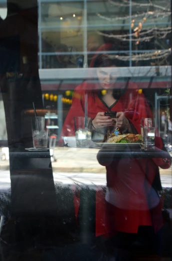 woman in red looking at cell phone through window