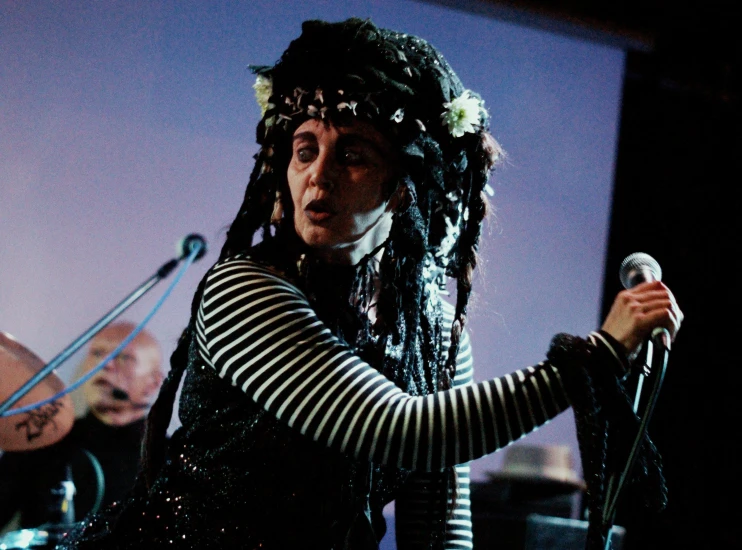 a woman wearing long hair standing behind microphones