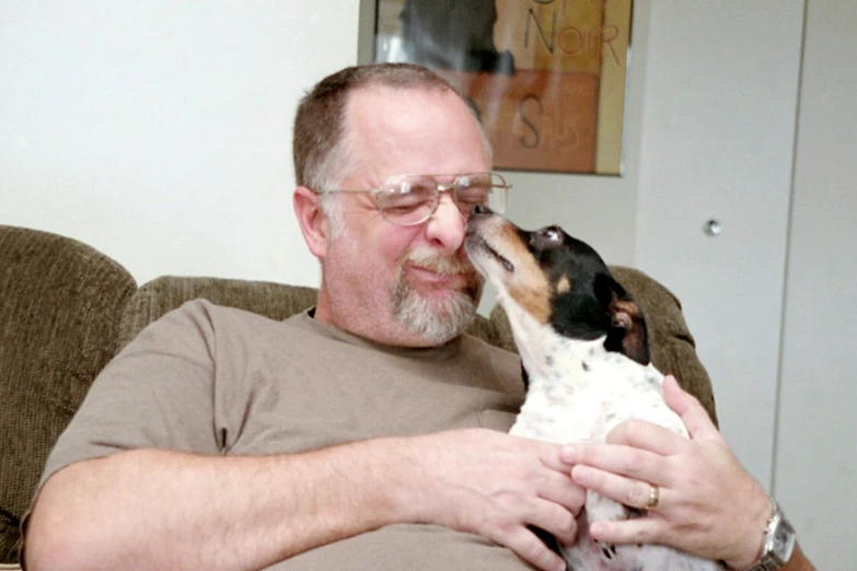 a man sitting in a chair petting a small dog