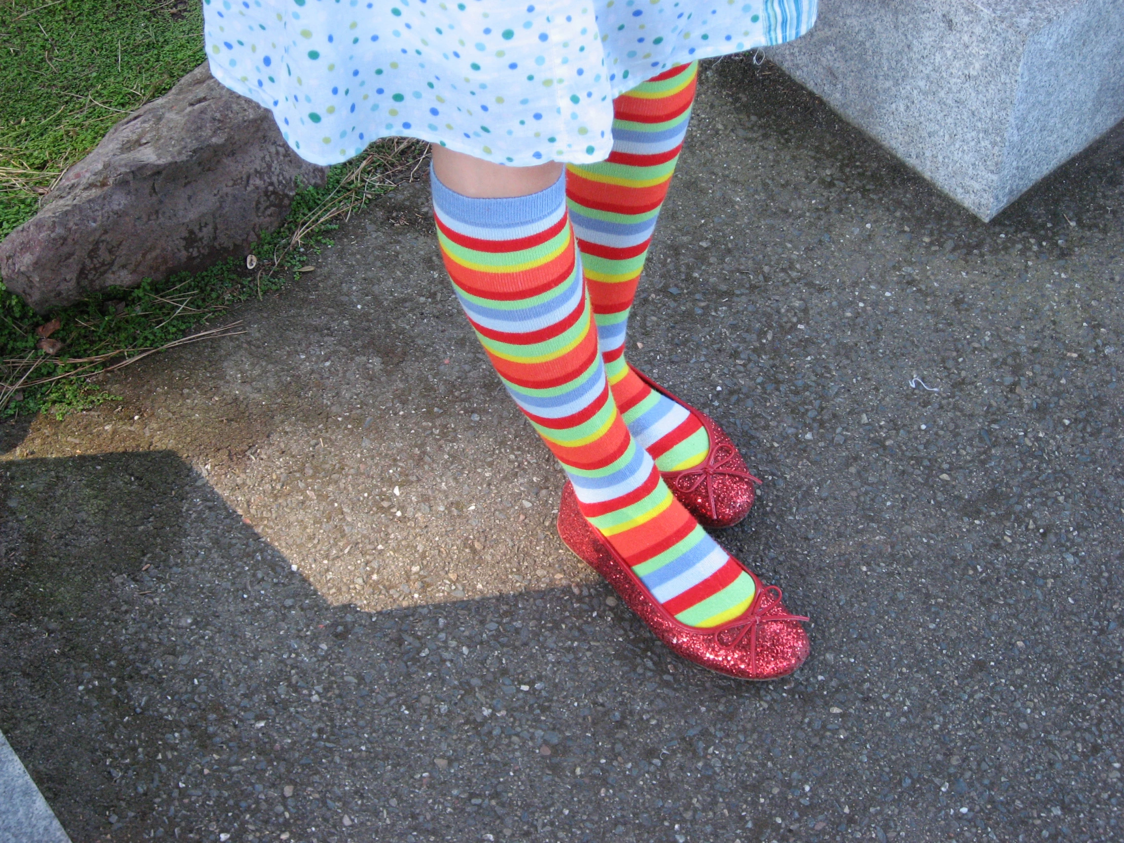 a girl in colorful socks standing on pavement next to concrete