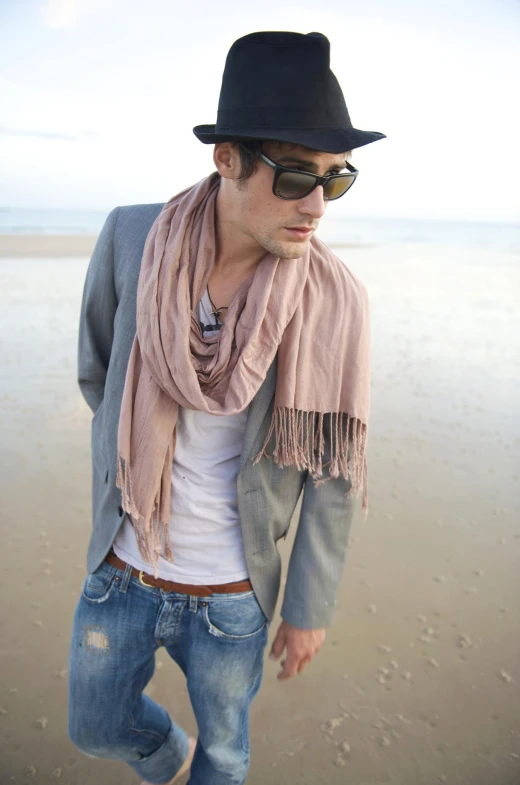 a man standing on top of a beach wearing a hat and scarf