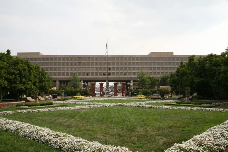 a large office building sits on a grassy lawn in front of a white flower garden