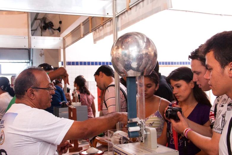 a group of people standing around a metallic object on top of a table