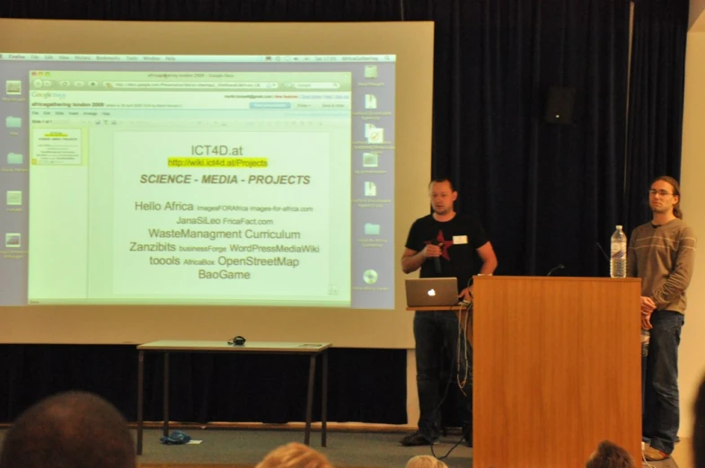 two people standing near a podium on top of a screen