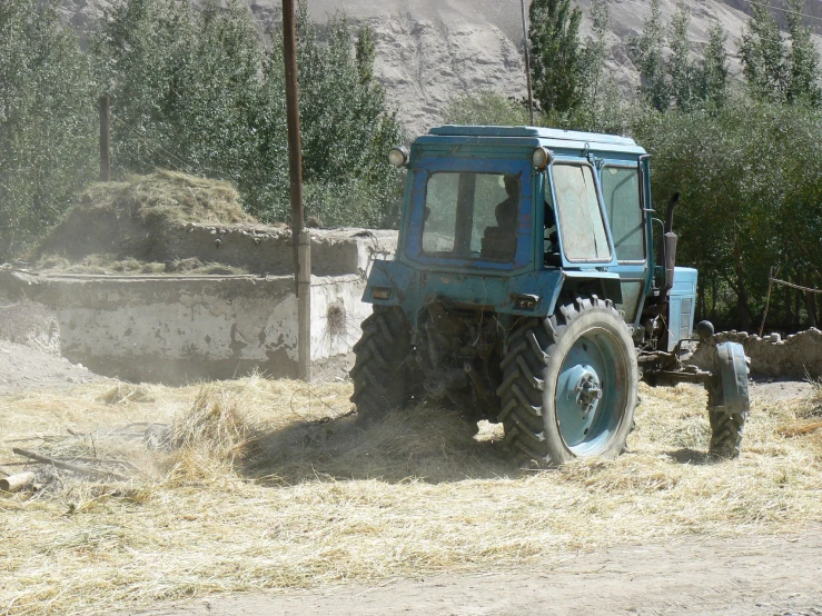 a farmer tractor that is driving away from some hay