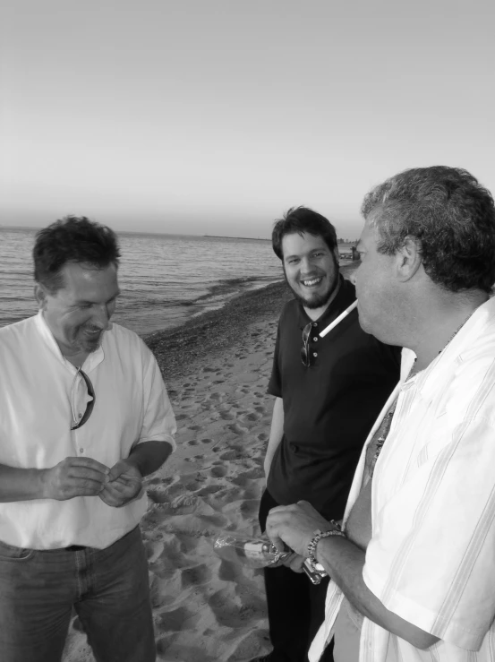 two men stand in front of the ocean and laugh while another man walks toward him