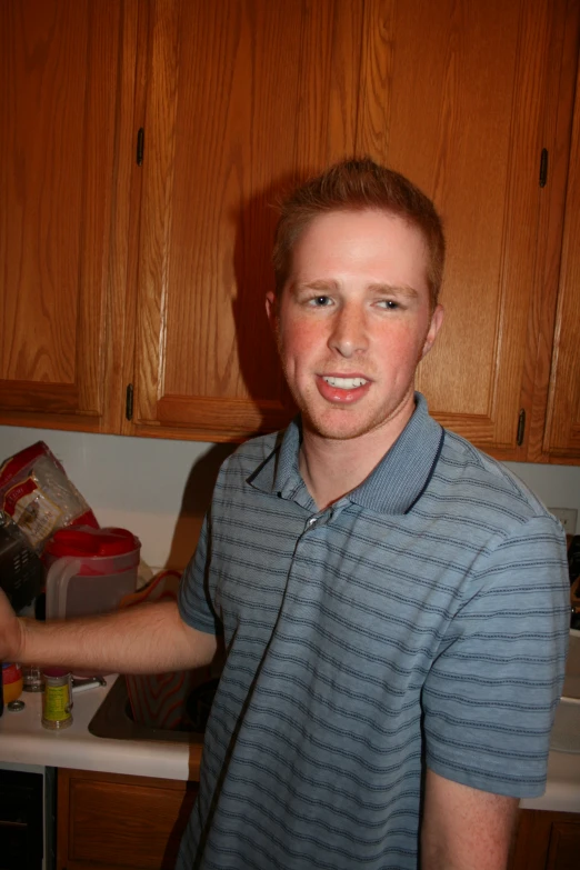 a smiling man standing in a kitchen next to brown cabinets