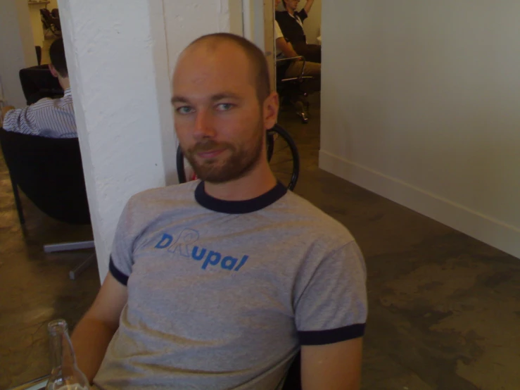 a bald man looking straight ahead in a grey and blue shirt