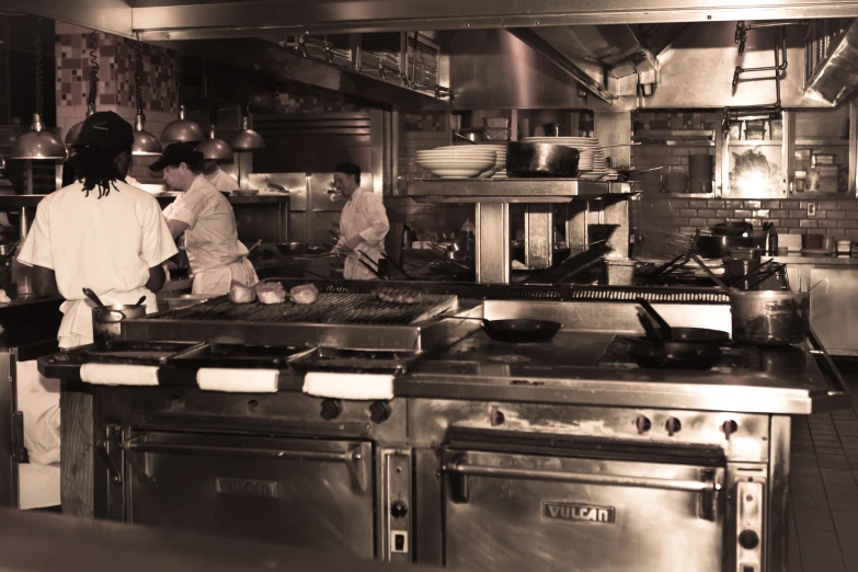 people working in a large kitchen behind the stove