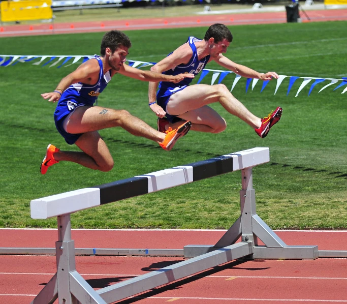 two men running over an obstacle hurdle in a track