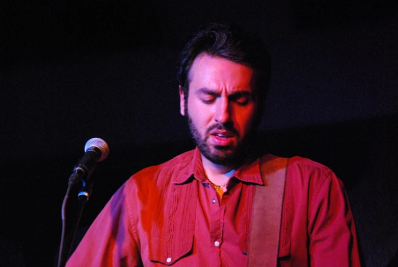 a man wearing a red shirt standing in front of a microphone