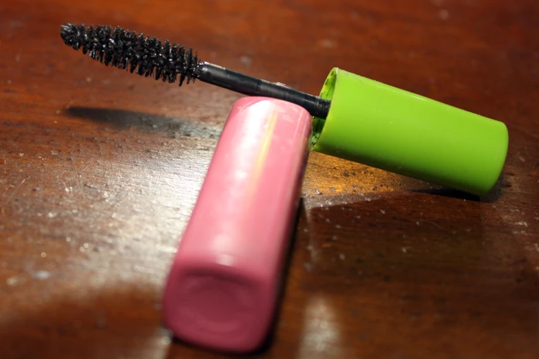 a bottle with a black mascara inside of it sitting next to a pink tube