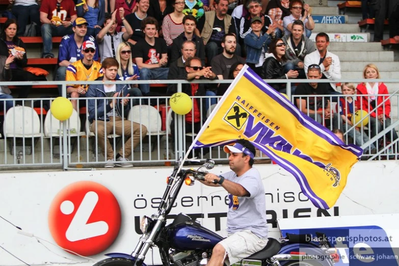 man on motorcycle with flags in front of spectators