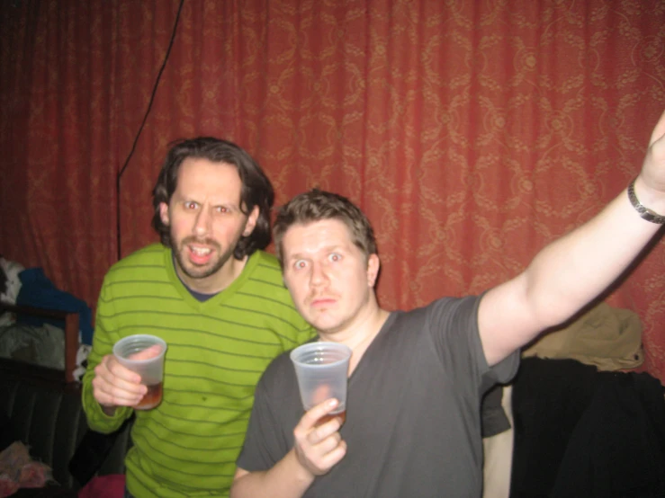 two men are holding drinks with their arms up