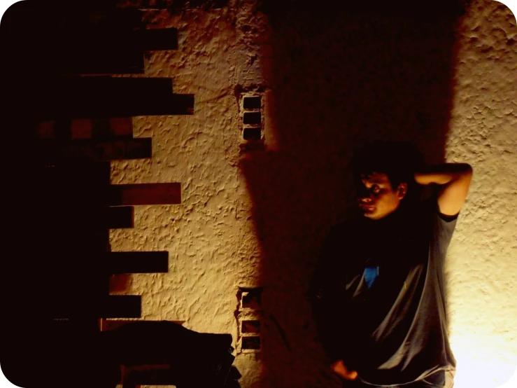 a boy leaning against a wall with his arm in his hair