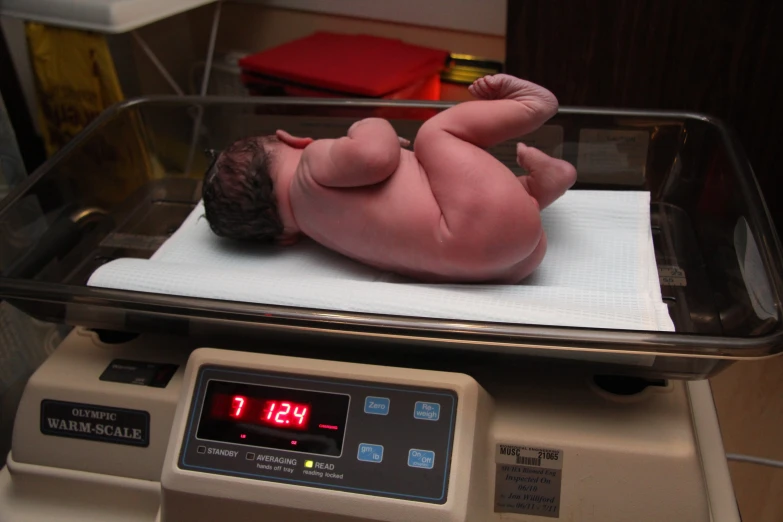 an infant laying on a scale in front of a clock