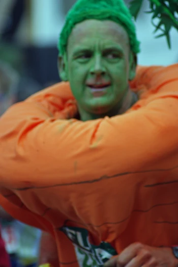 a man with green hair is dressed in an orange sweatshirt