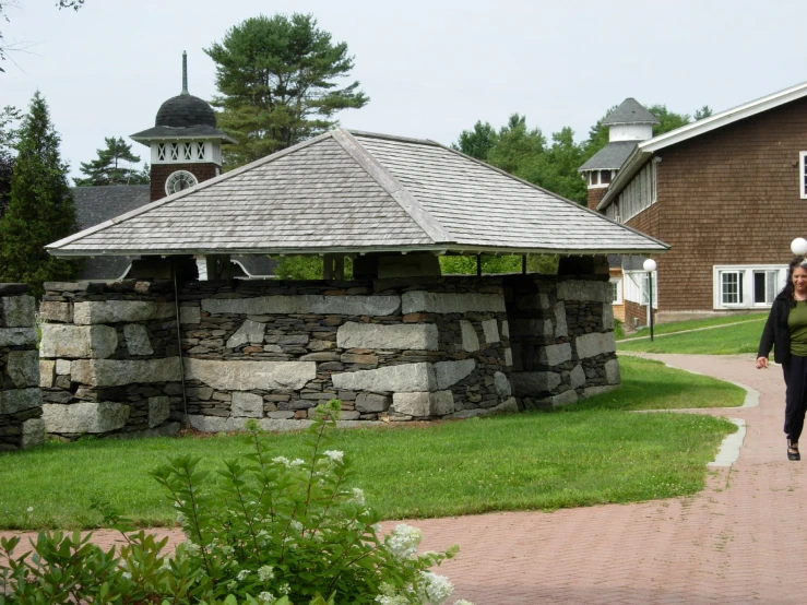 a woman walks past a stone structure near buildings