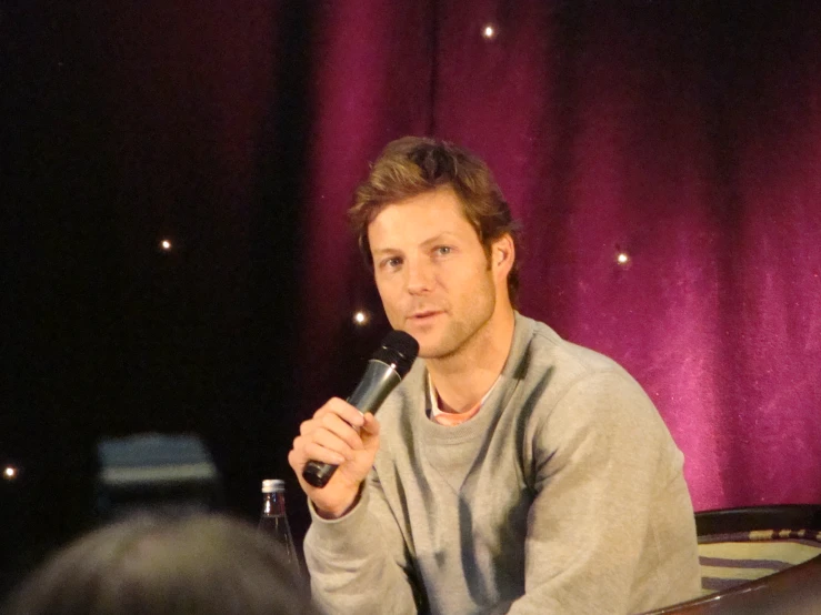 a young man sits on a stage and holds a microphone