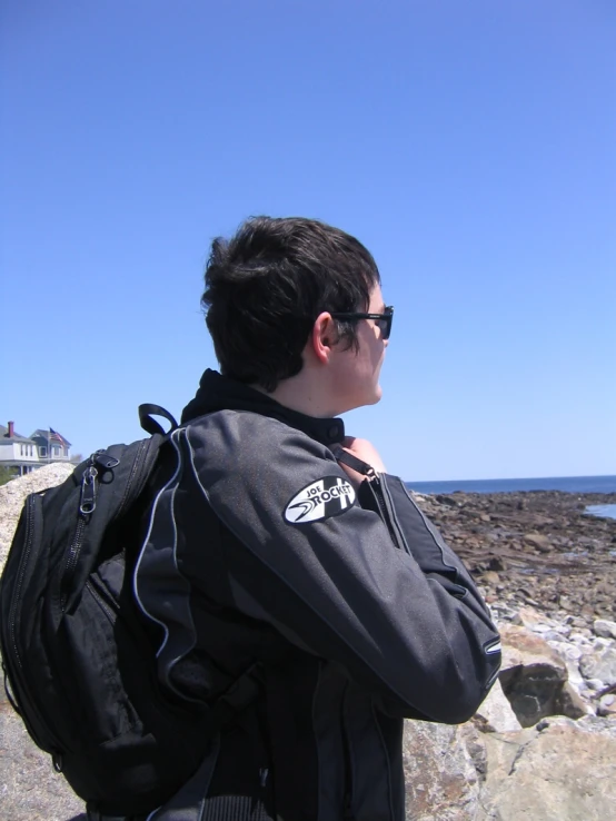 a person in black jacket on rocks near water