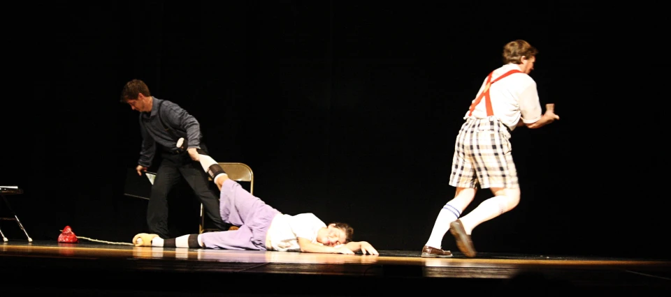 three actors are performing on stage one is injured, and the other is lying on the ground