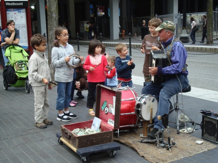 a man plays a musical instrument while children stand around