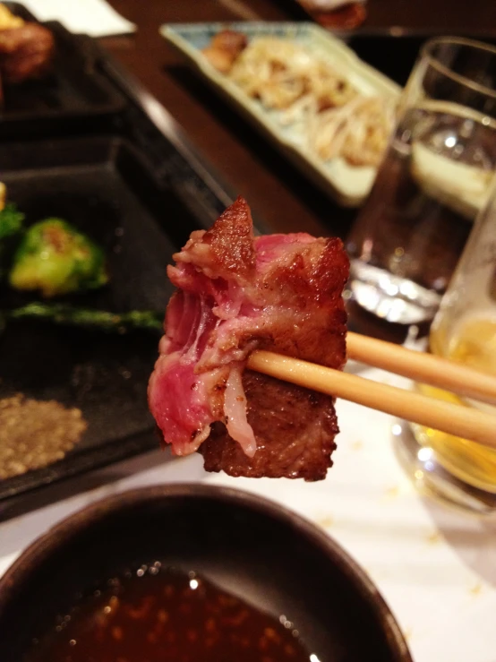 a close up of chopsticks holding meat with vegetables and dipping sauce