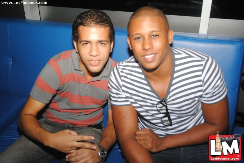 two men pose for the camera on a blue couch