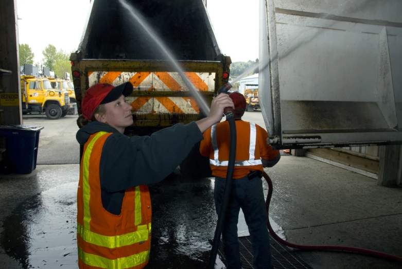 two people in orange vests holding a hose