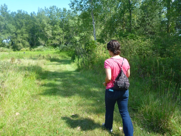 a woman in a field walking toward some trees