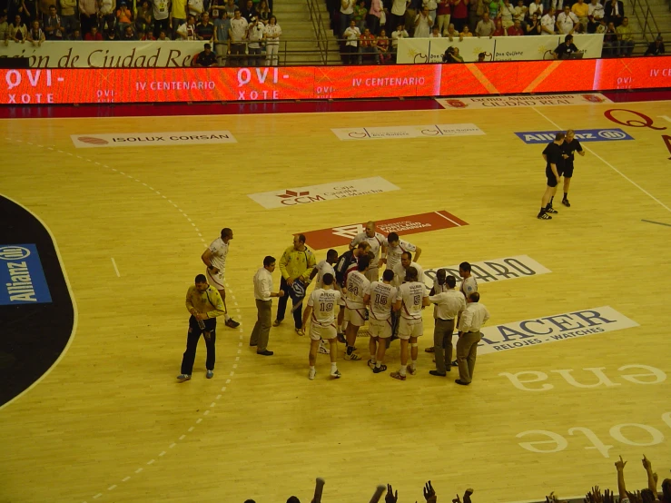 a group of men are talking to each other in front of an empty basketball court