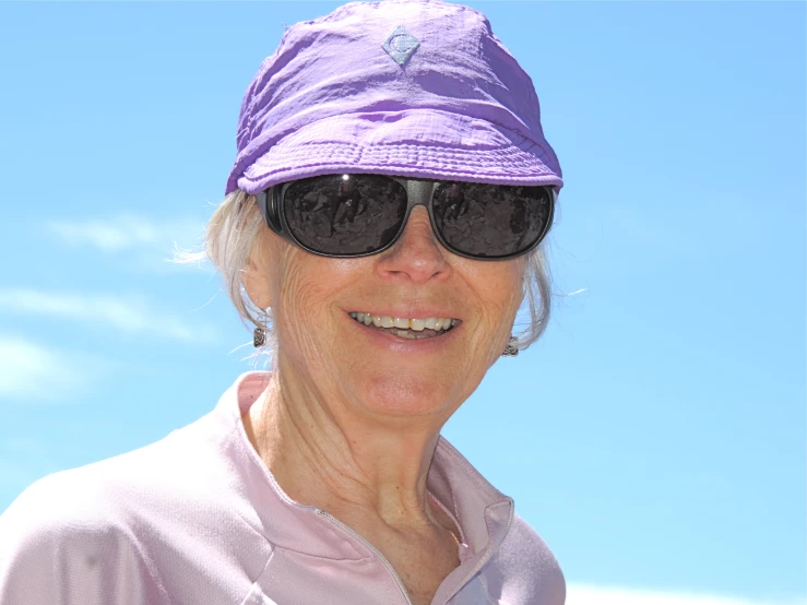 an old woman in sunglasses and a purple hat smiling