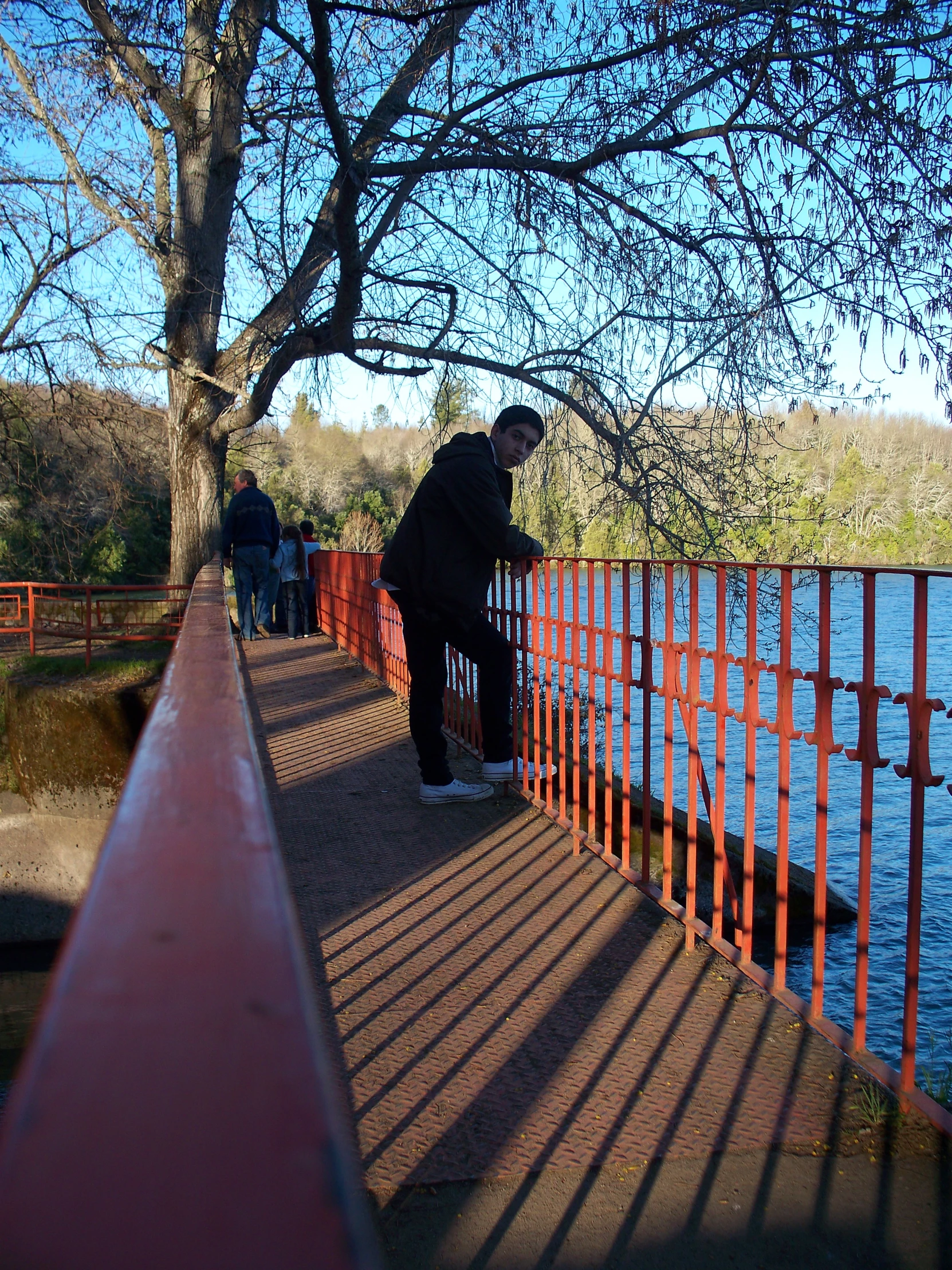 people walking down the sidewalk near water and orange railing