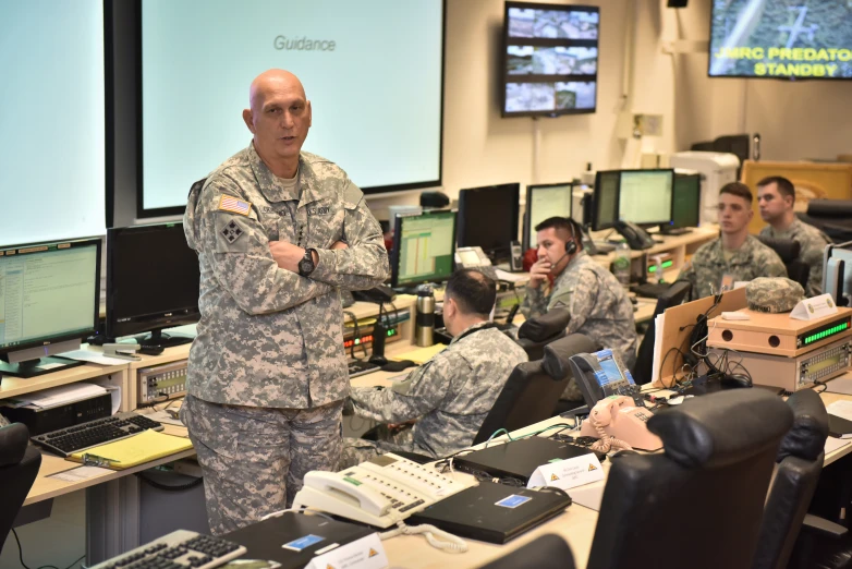 soldiers in uniforms working on computers, and the military man is standing with his arms crossed