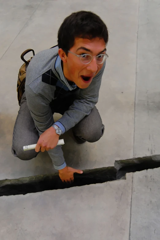 a guy in glasses and a gray suit crouches with his hands on the ground while wearing glasses