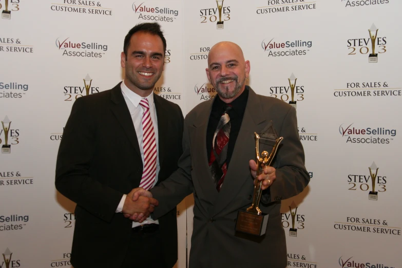 two people standing in front of a white wall holding up some awards