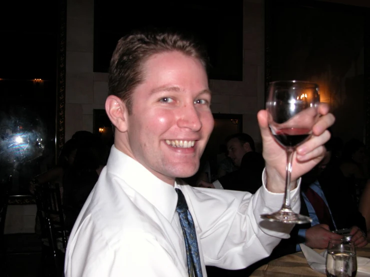 a man smiles while holding a wine glass