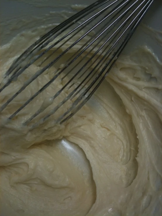 a white mixer filled with cream next to a metal wire whisk