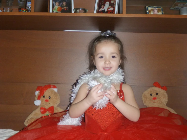 a little girl dressed in a red gown is standing on a bed