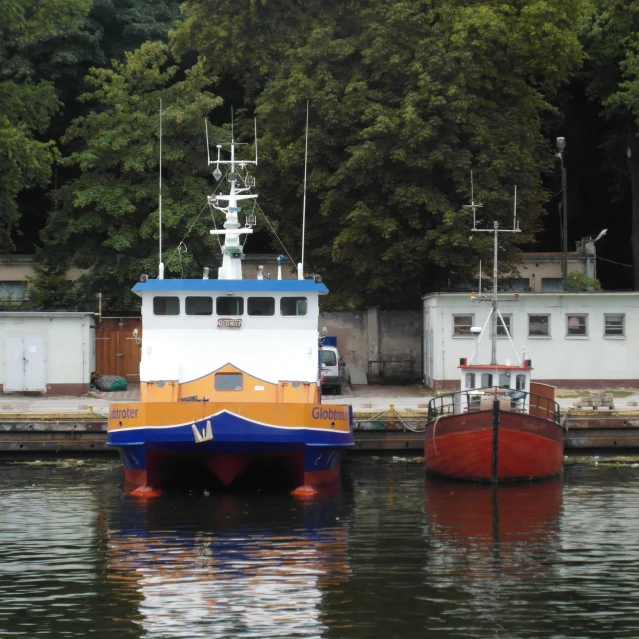 two boats sit at the dock beside some trees