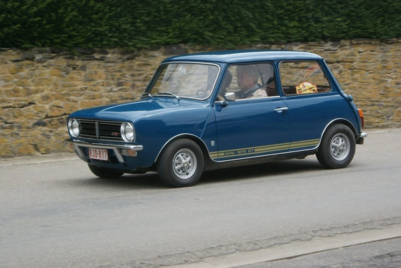 a small car driving on the street by some wall